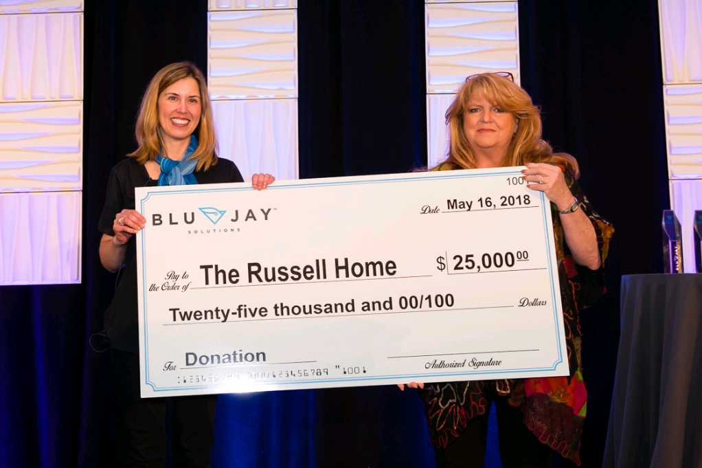 Two team members at The Russel Home holding a large donation check
