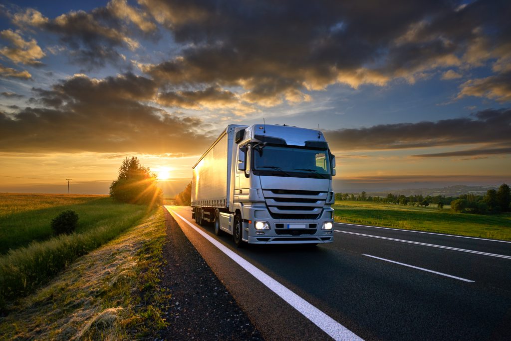 truck driving down a rural highway while the sun sets