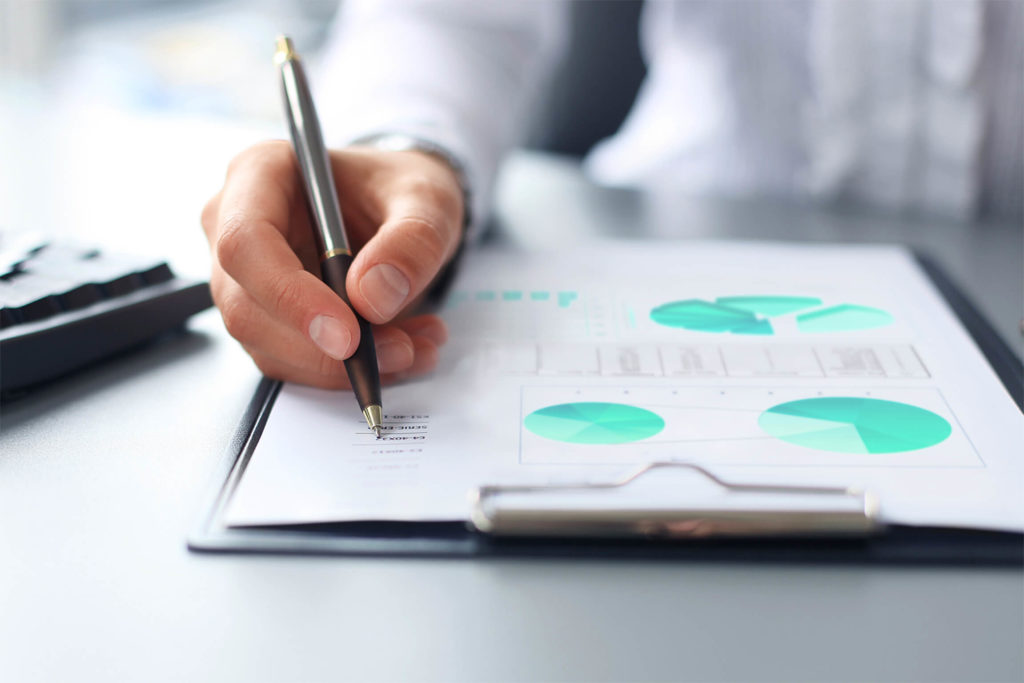 man writing on a report on a clipboard with various graphs and charts